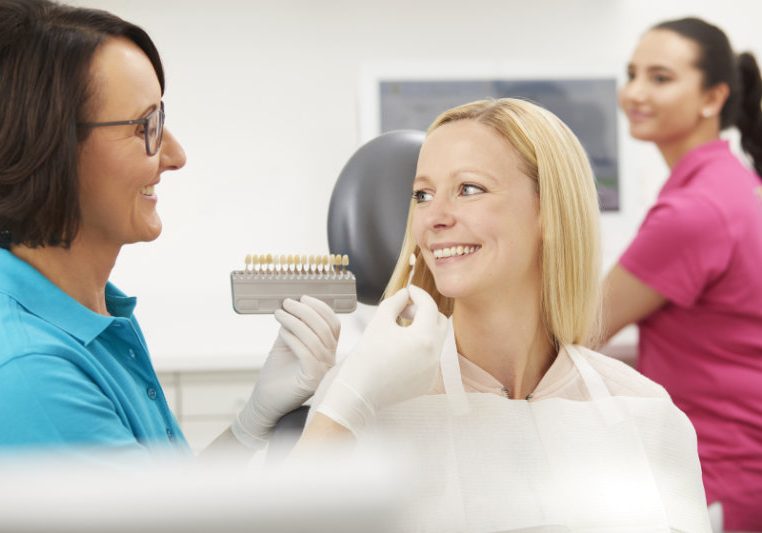 Frau Rösen macht Farbabgleich mit Zähnen einer Patientin